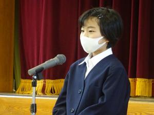 緊張した面持ちでマイクの前に立つ紺の上着を着用した入所児童の写真