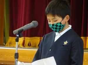 手に持って広げている原稿用紙に視線を落としているチェックのマスクを着けた入所児童の写真
