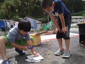 虫眼鏡で火おこしする留学児童の写真