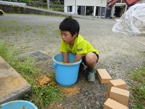 バケツで土をこねる留学児童の写真