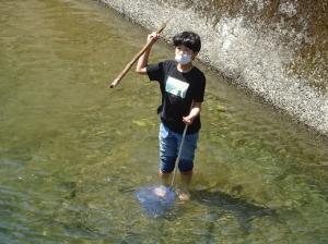 ひざ下まで水に浸かりながら魚釣りをする留学児童の写真