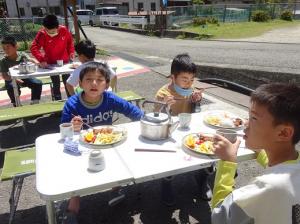 屋外で日の光を浴びながらお昼ご飯を食べる留学児童の写真