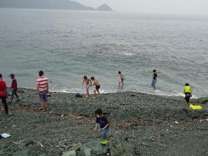 雨の合間に海に足だけつける留学児童の写真