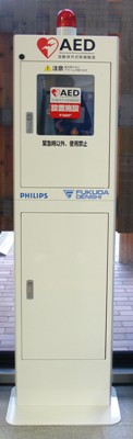 AED（自動体外式除細動器）の写真。縦に長い白い箱に入っており、上にパトランプがついている。