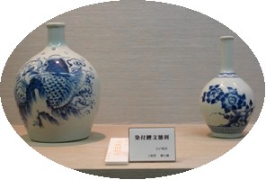 白を基調に、青色で魚や花の絵が描かれている、2つの砥部焼が展示されている様子を写した写真
